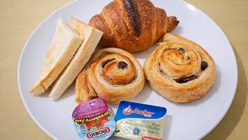 Um prato com um croissant, duas fatias de pão, dois doces e dois pacotes de manteiga.