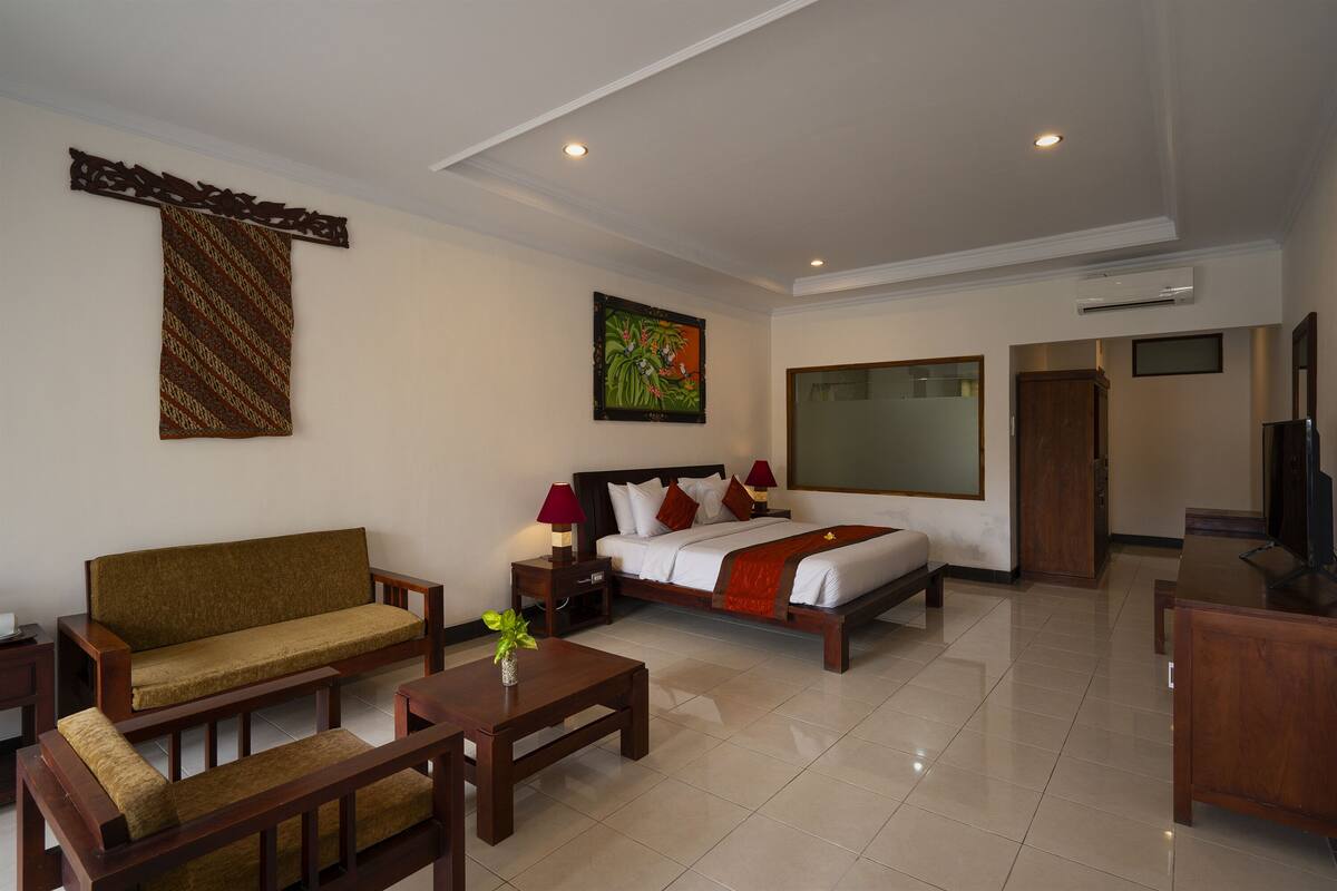 A hotel room with a sofa, a bed with a red blanket, a wooden desk, and a TV.