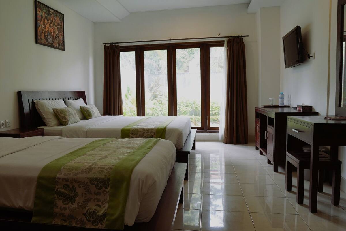 A hotel room with two beds, a desk, a television, and a window with curtains.