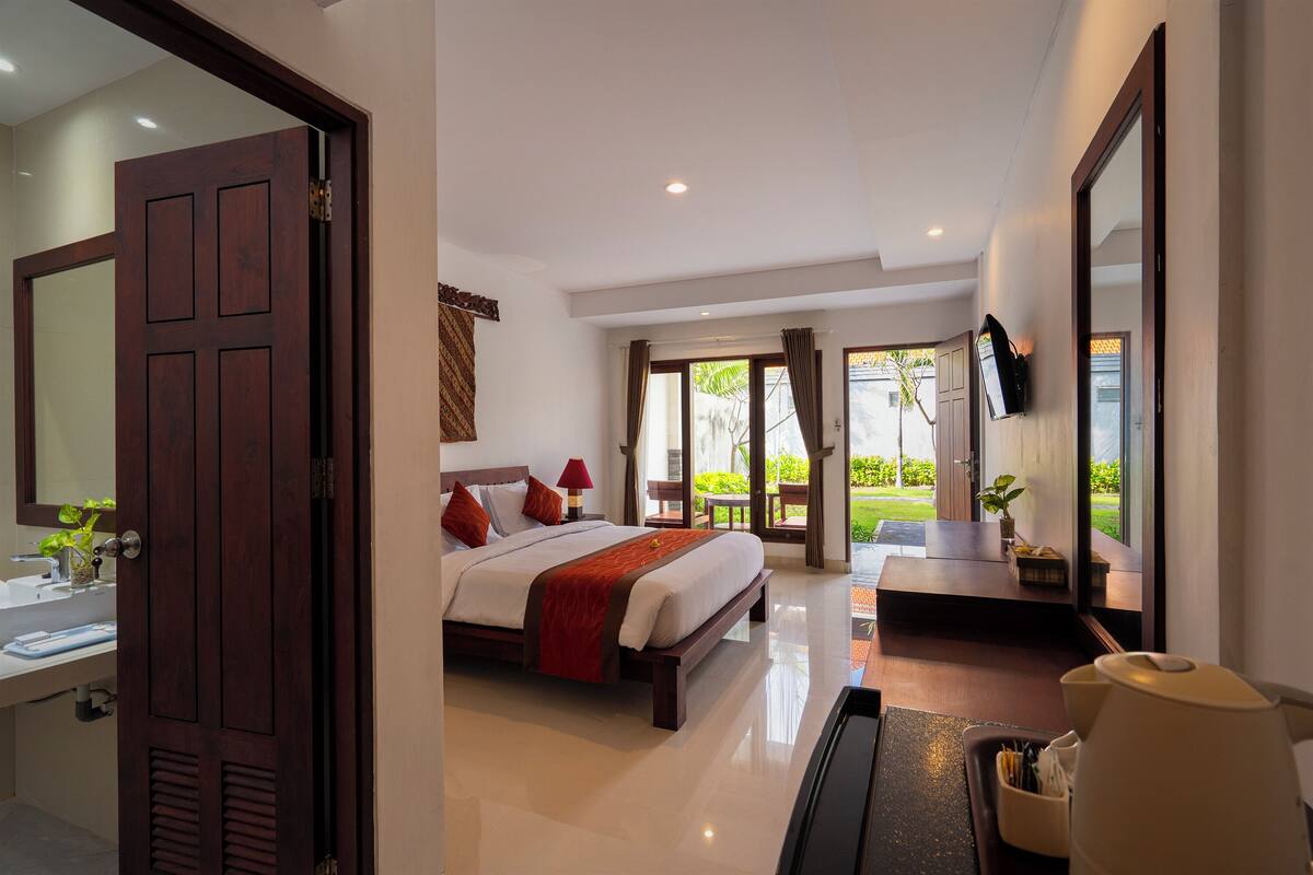A hotel room with a bed, bedside table, TV, and a view of the garden.