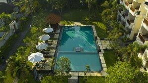 Vista aérea de un resort con piscina rectangular rodeada de sillas de descanso y sombrillas, un pequeño pabellón y exuberante vegetación.
