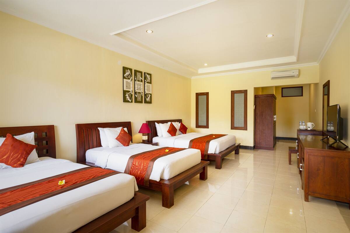 A hotel room with three beds, a wooden desk, a TV, and a mirror.