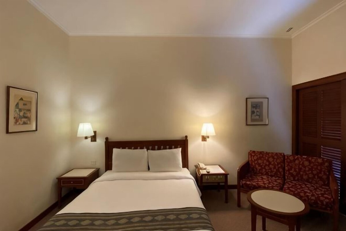 Een hotelkamer met een bed, twee bedlampen, een stoel, een klein tafeltje en een deur met een houten paneel.