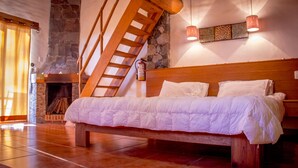 A bedroom with a wooden bed, a stone fireplace, a wooden staircase, and a hanging light fixture. - Cabañas Monterra Tapalpa (Tapalpa)