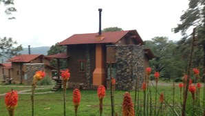 A stone building with a red roof, surrounded by tall grass and red flowers. - Cabañas Monterra Tapalpa (Tapalpa)