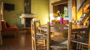A dining area with a round wooden table and chairs, a stone fireplace, and a staircase. - Cabañas Monterra Tapalpa (Tapalpa)