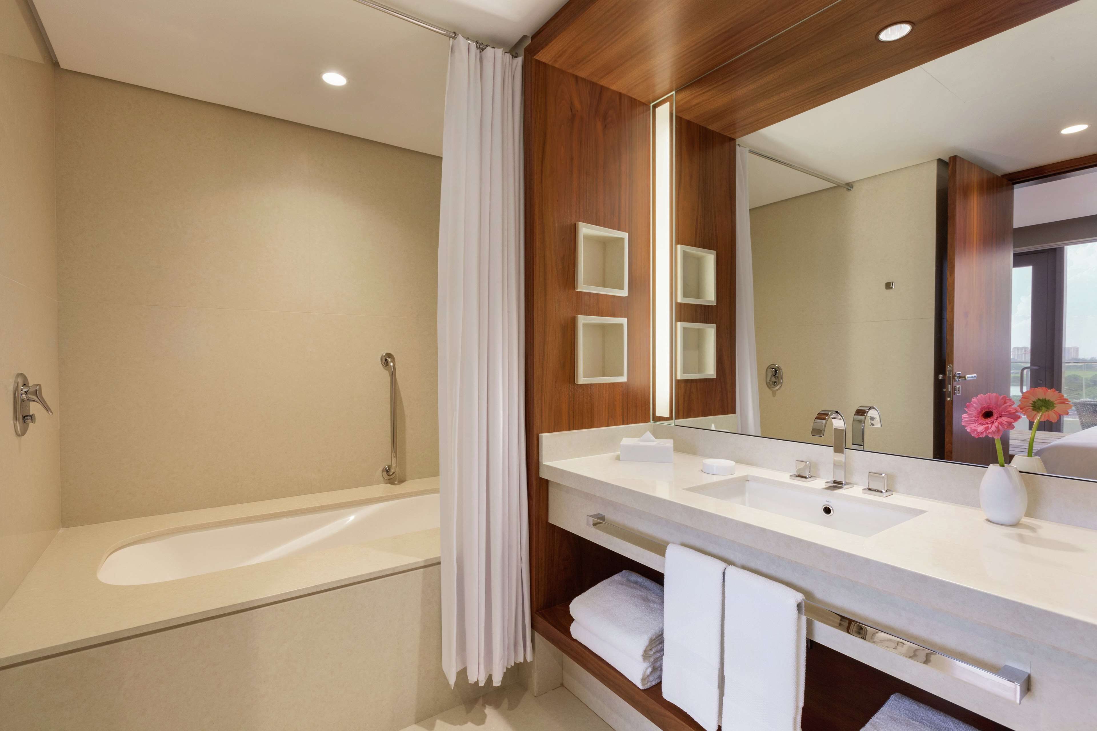 Un baño moderno con bañera, dos lavamanos, un tocador con almacenamiento, un espejo y una cortina de ducha.
