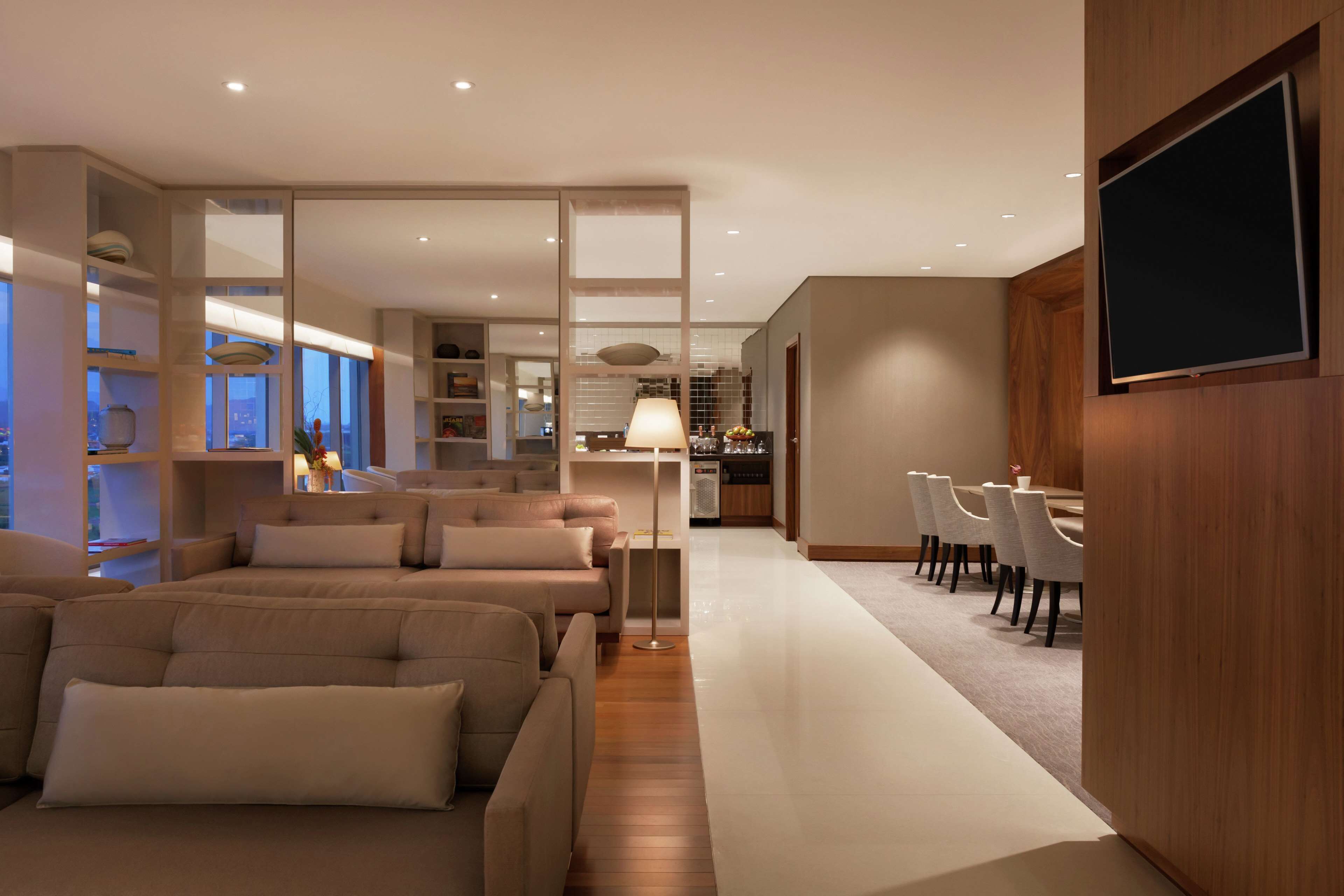 A modern living room with a sofa set, a dining area with chairs, and a TV mounted on the wall.