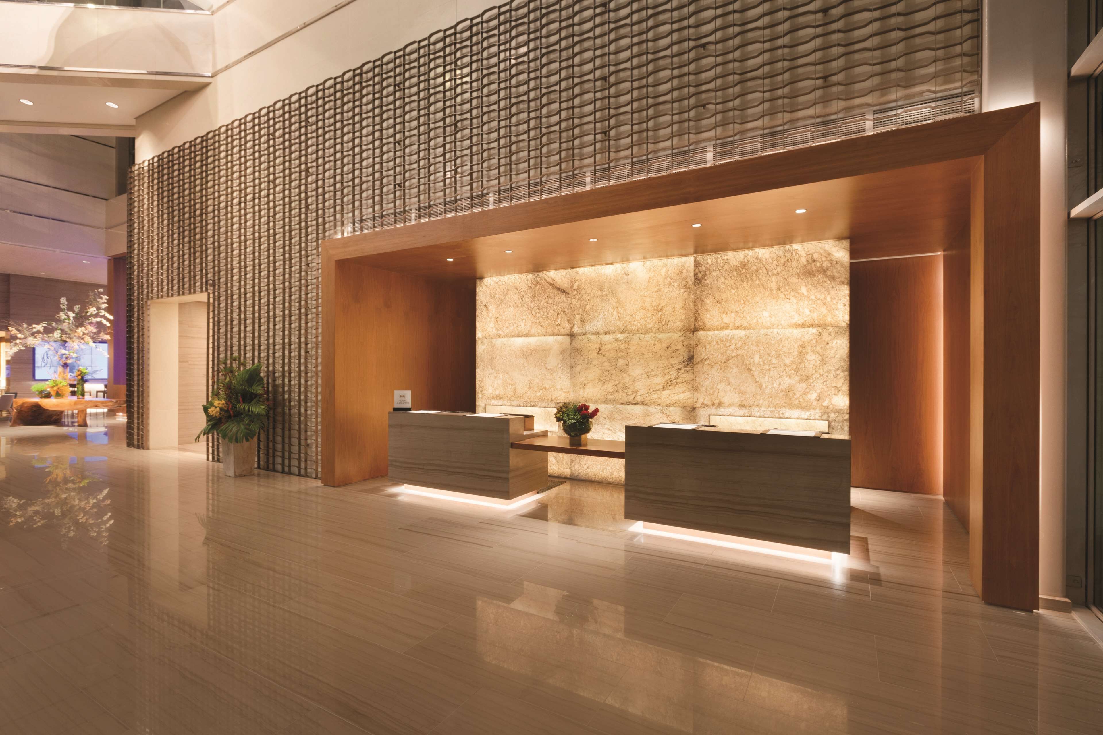 A modern reception area with a marble wall, wooden reception desk, and a decorative plant.