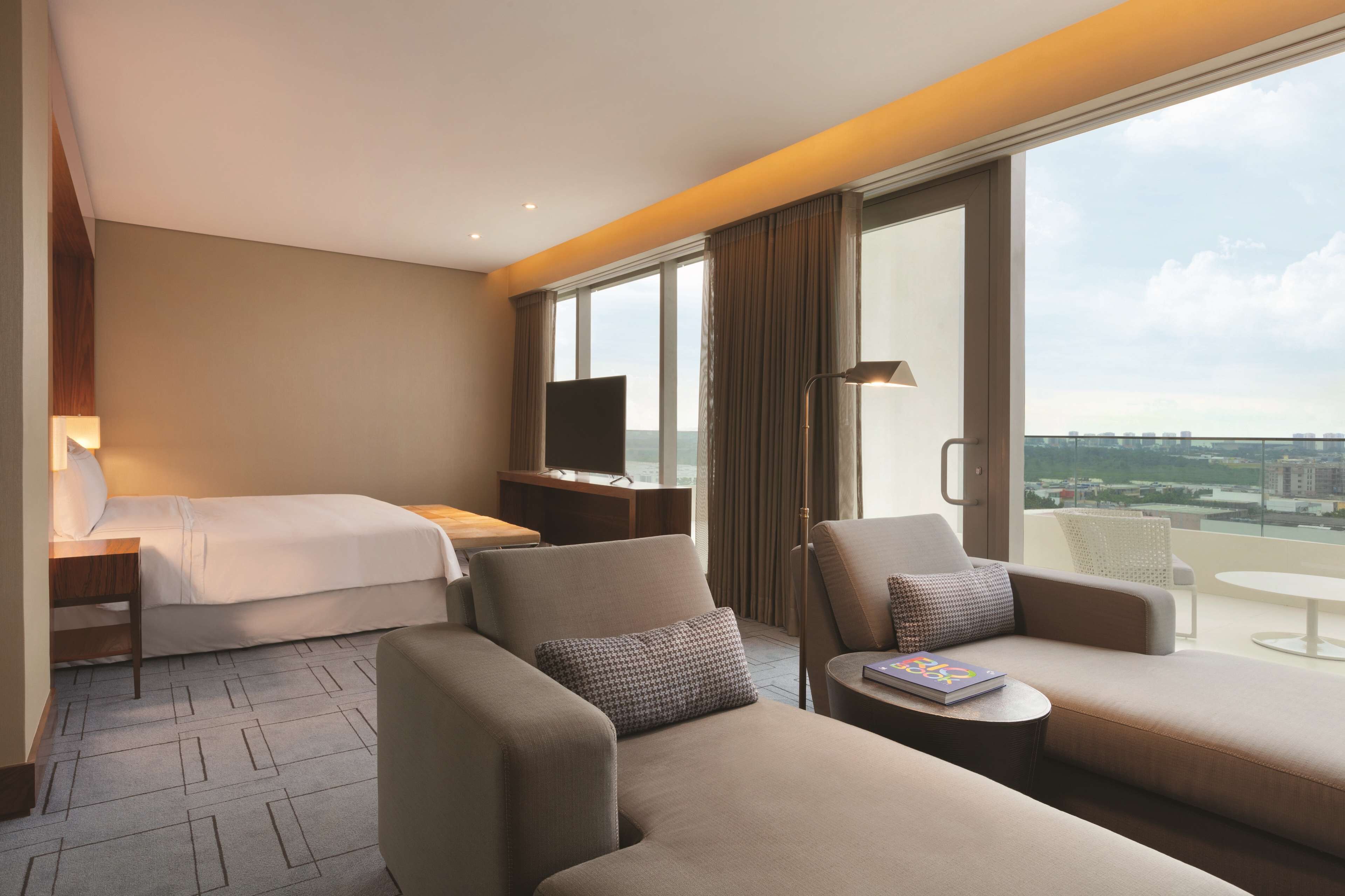 Une chambre d’hôtel comprenant un lit, deux canapés, une petite table, un téléviseur et un balcon avec vue sur la ville.
