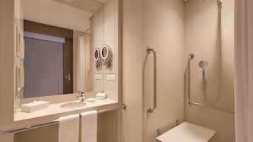 A modern bathroom with a large mirror, two sinks, a shower with a handheld showerhead, and a grab bar.