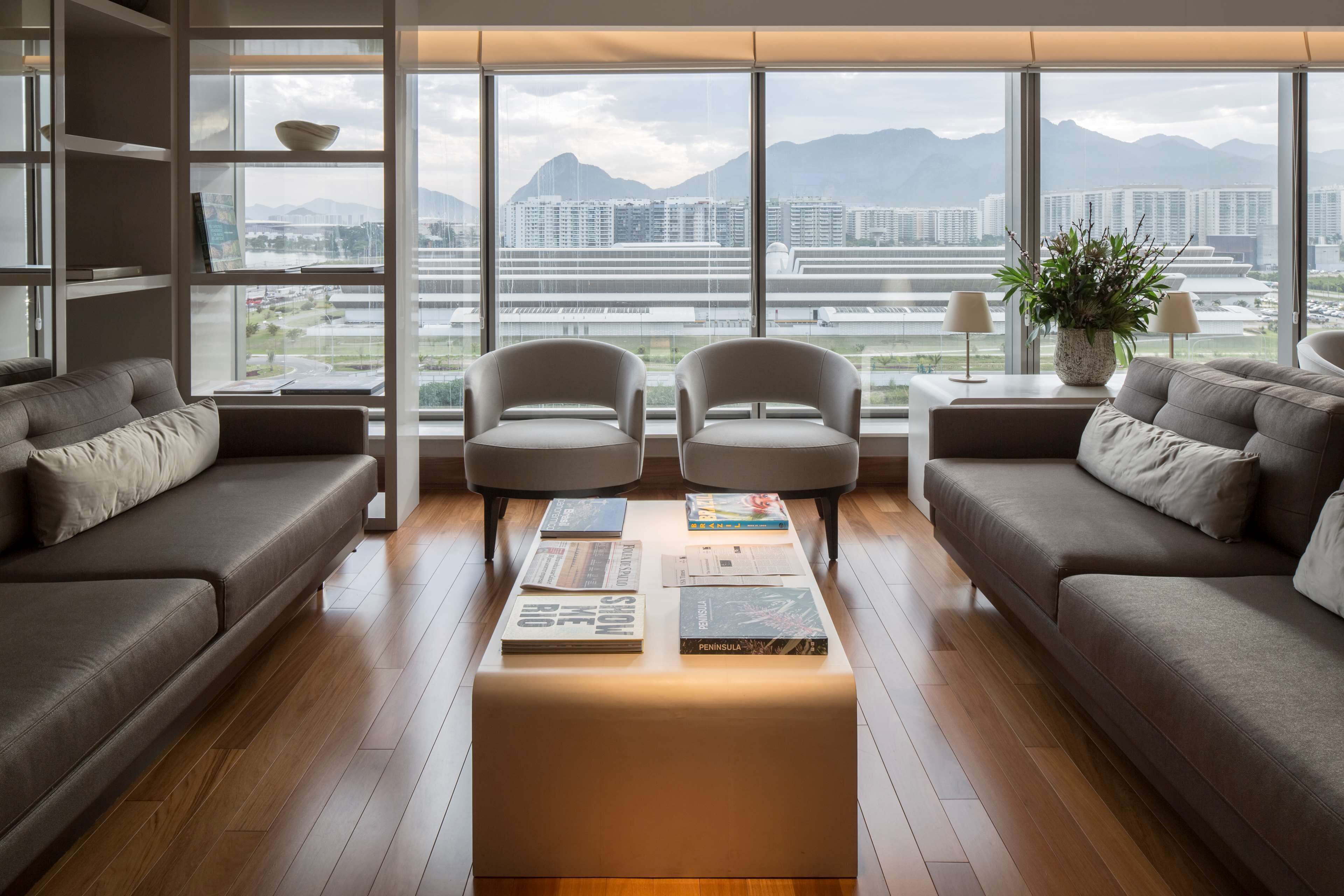 A modern living room with a large window, two sofas, a coffee table with books, and a potted plant.