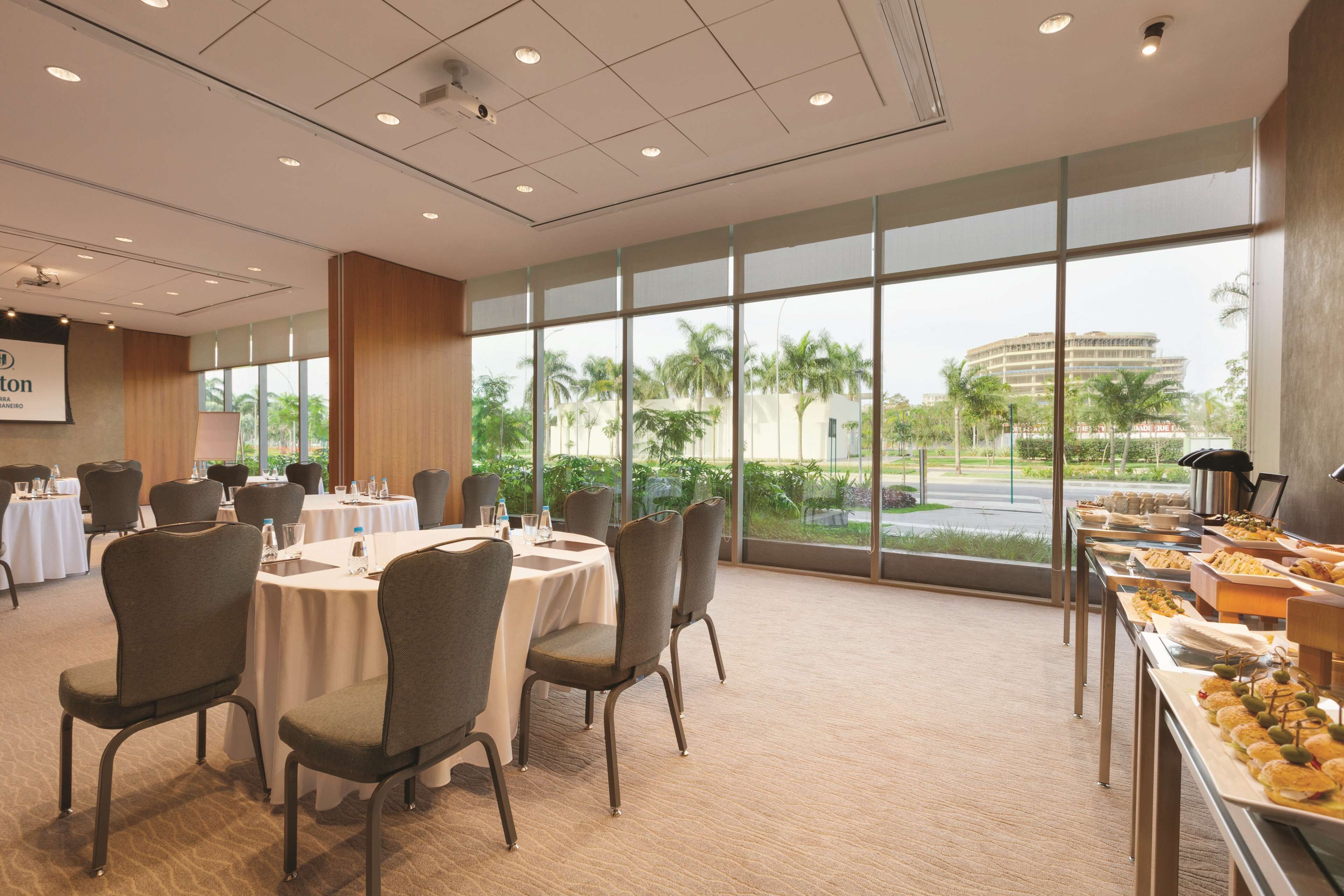 A conference room with round tables, chairs, and a buffet area with food.