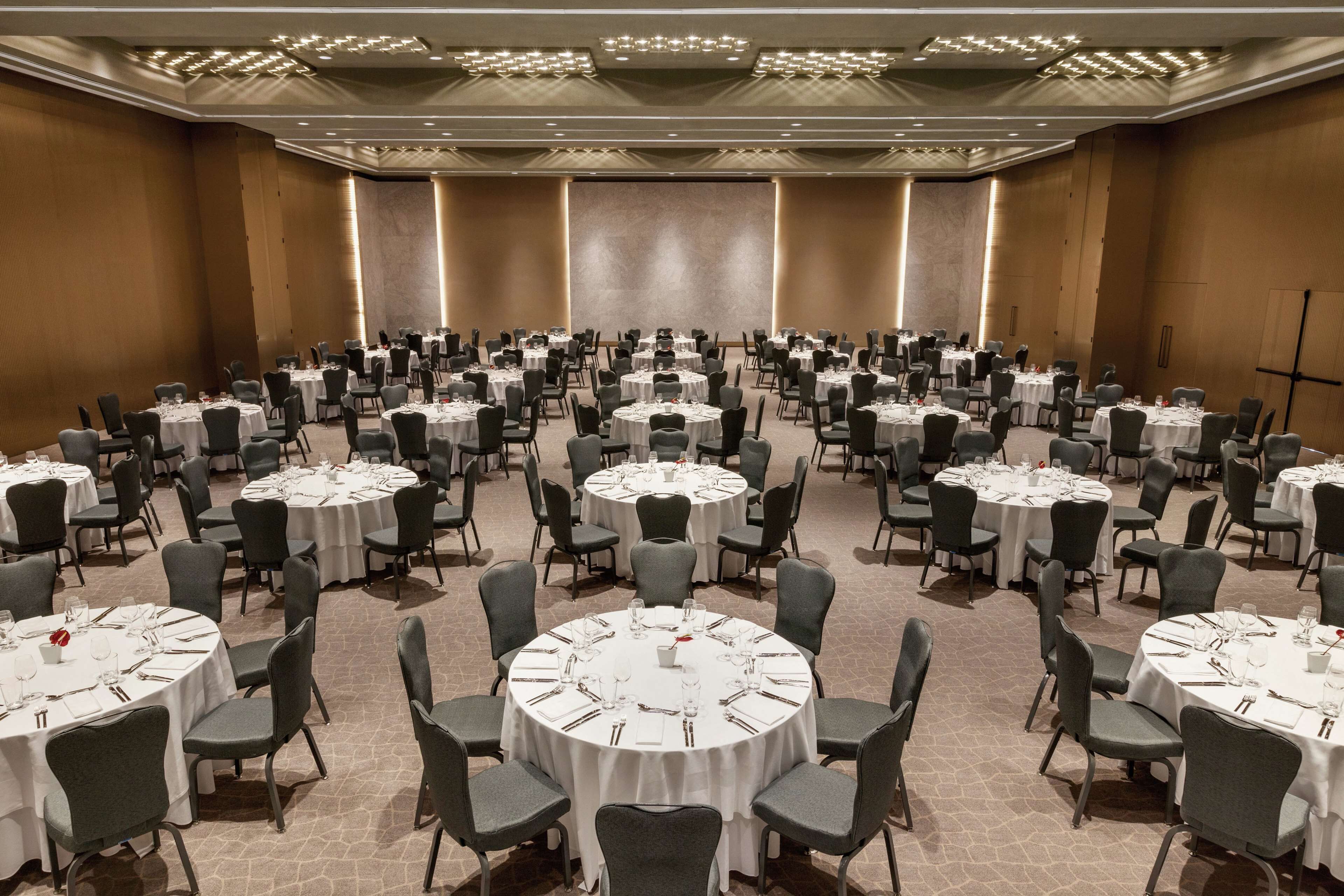 A large conference room with multiple round tables set for dining, equipped with chairs and table settings.