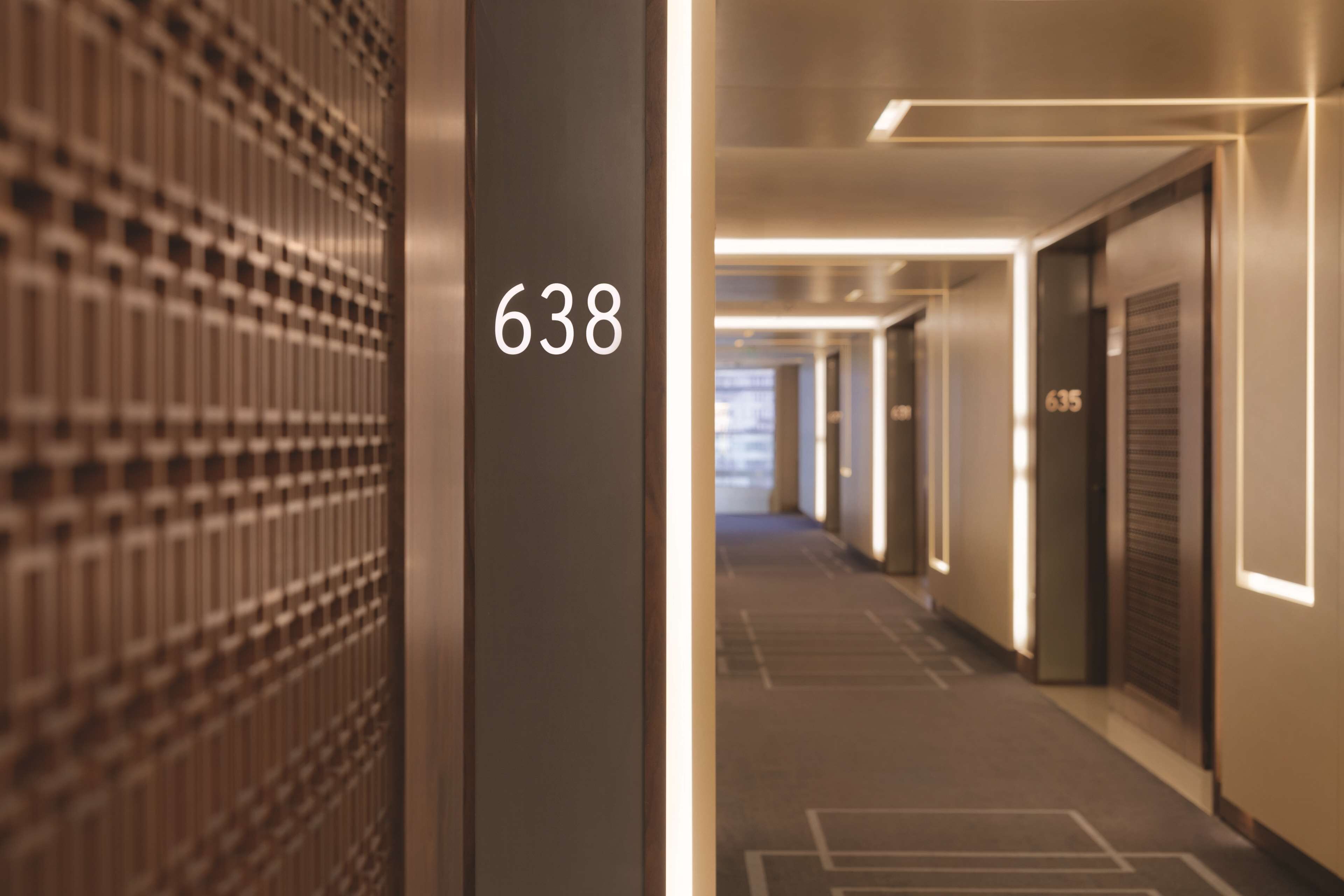 A hallway with a number 638 sign, indicating a room number. The hallway has a modern design with a patterned wall on the left and doors on the right.