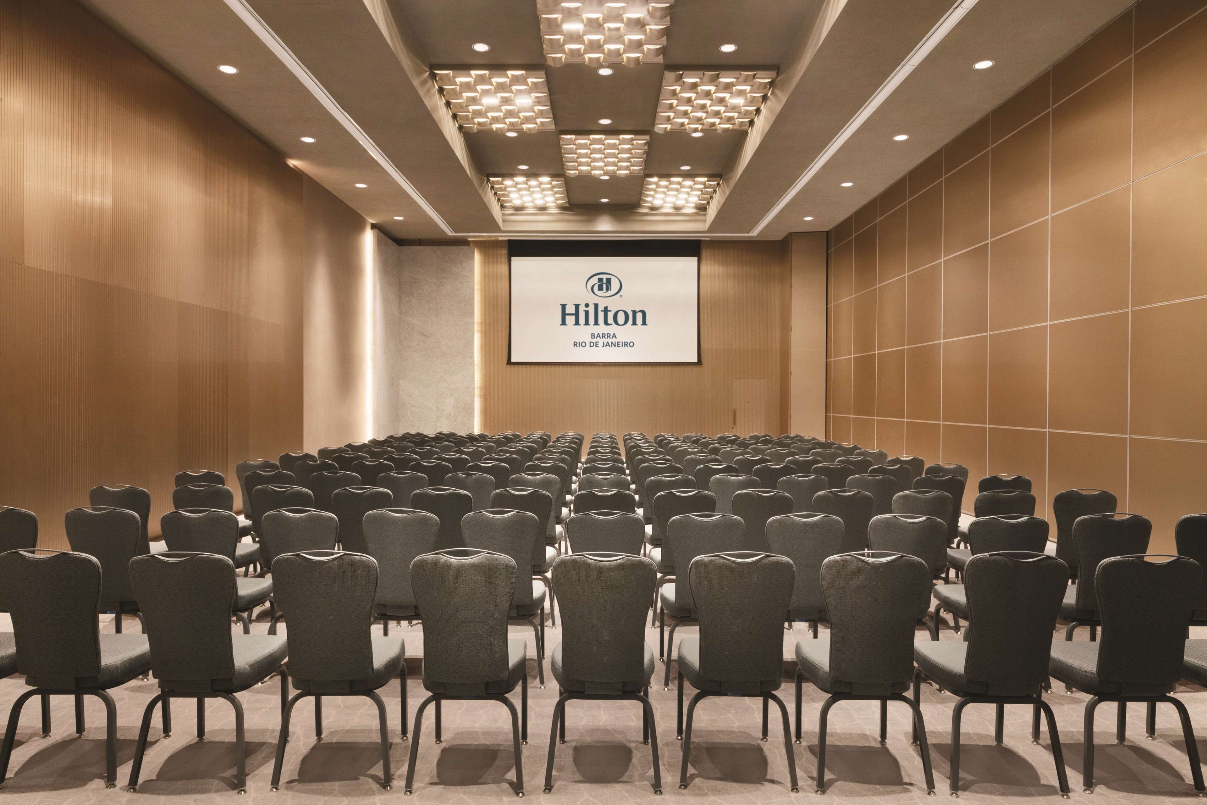 Un salón de conferencias con hileras de sillas orientadas hacia una pantalla que muestra el logotipo de Hilton.