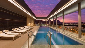 A rooftop pool with sun loungers and a city view at dusk. - Hilton Barra Rio De Janeiro (Rio de Janeiro)