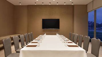 Un salón de conferencias con una larga mesa, sillas, un televisor de pantalla plana y una ventana con vistas.