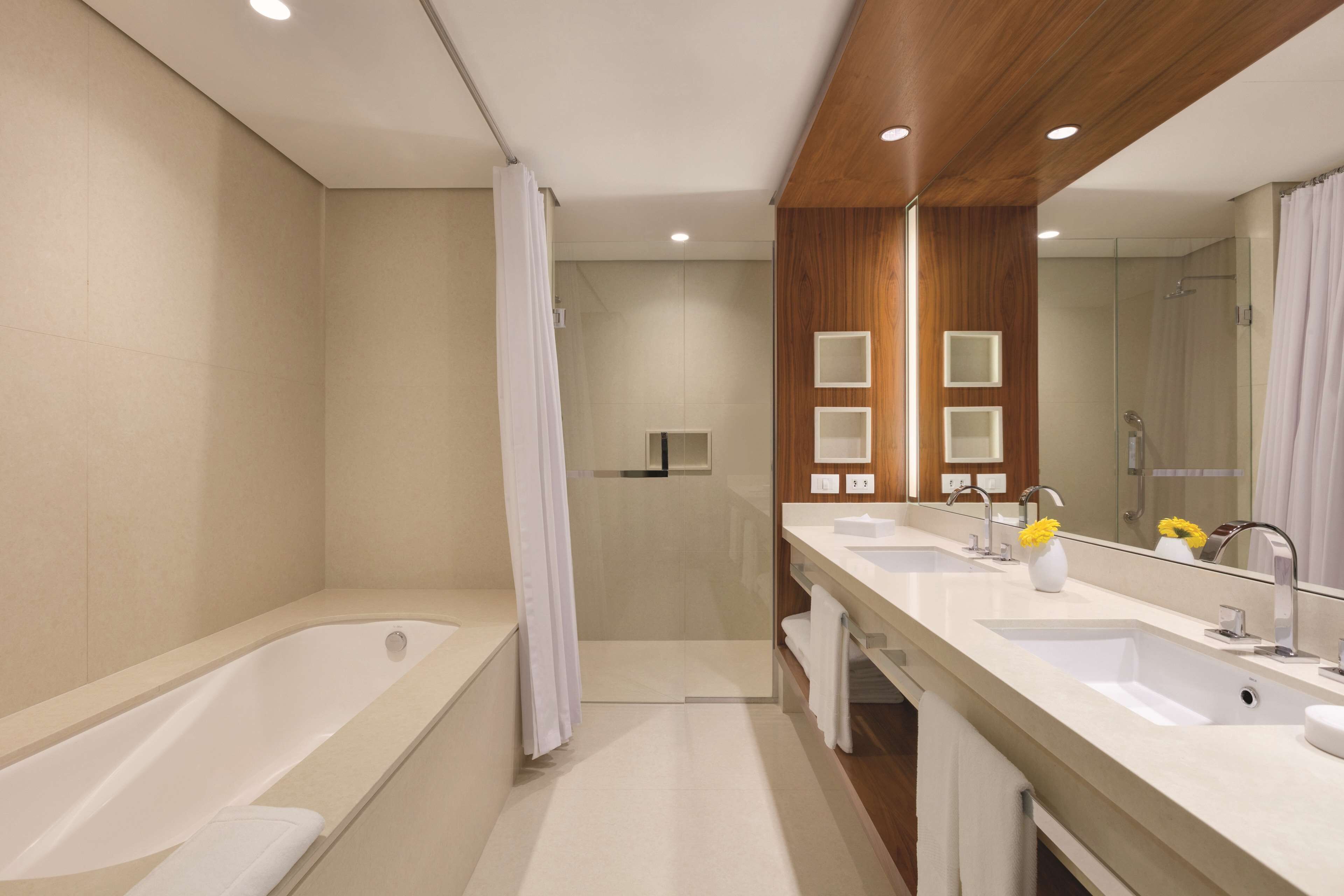 A modern bathroom with a bathtub, two sinks, a shower, and a large mirror.
