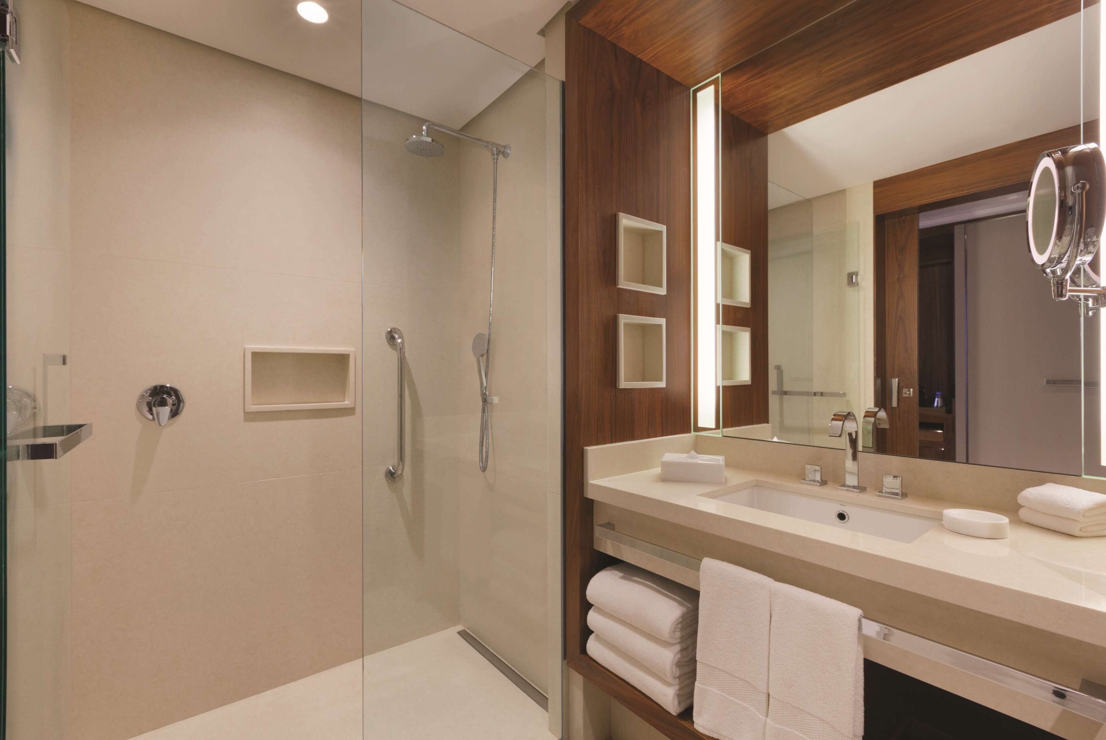 A modern bathroom with a glass-enclosed shower, a large mirror, and a vanity with multiple sinks and towel racks.