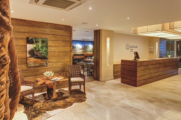 Un espace d’accueil avec un comptoir de réception en bois, un coin salon avec des chaises et une table, et un tableau représentant un paysage accroché au mur.