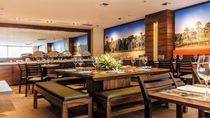 Un restaurant avec des tables et des chaises en bois, une grande fresque murale et un bar situé au fond de la salle.