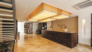 Un espace d’accueil d’hôtel au design moderne, comprenant un comptoir d’accueil, un escalier et un mur décoratif.