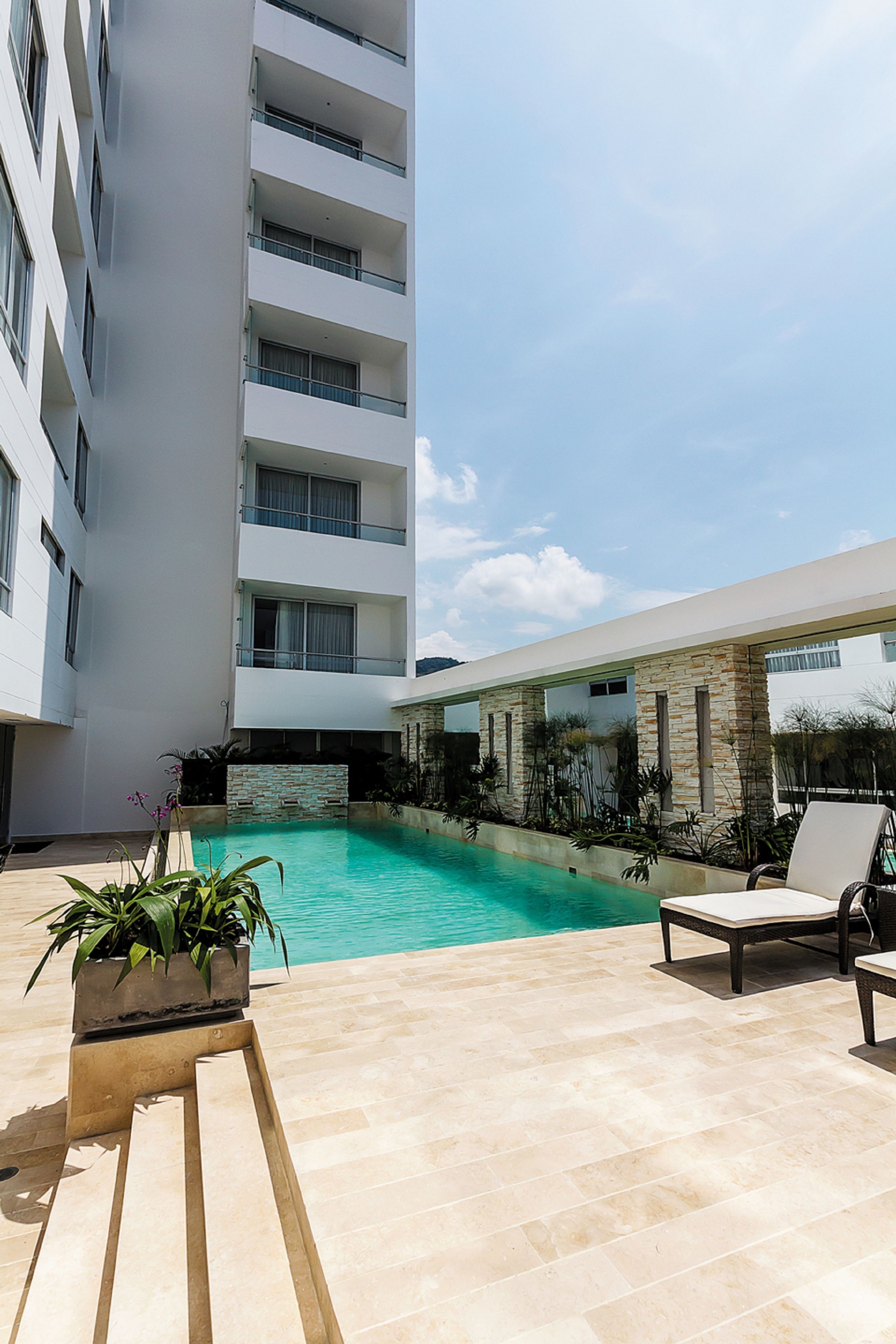 A modern building with a pool, lounge chairs, and potted plants.
