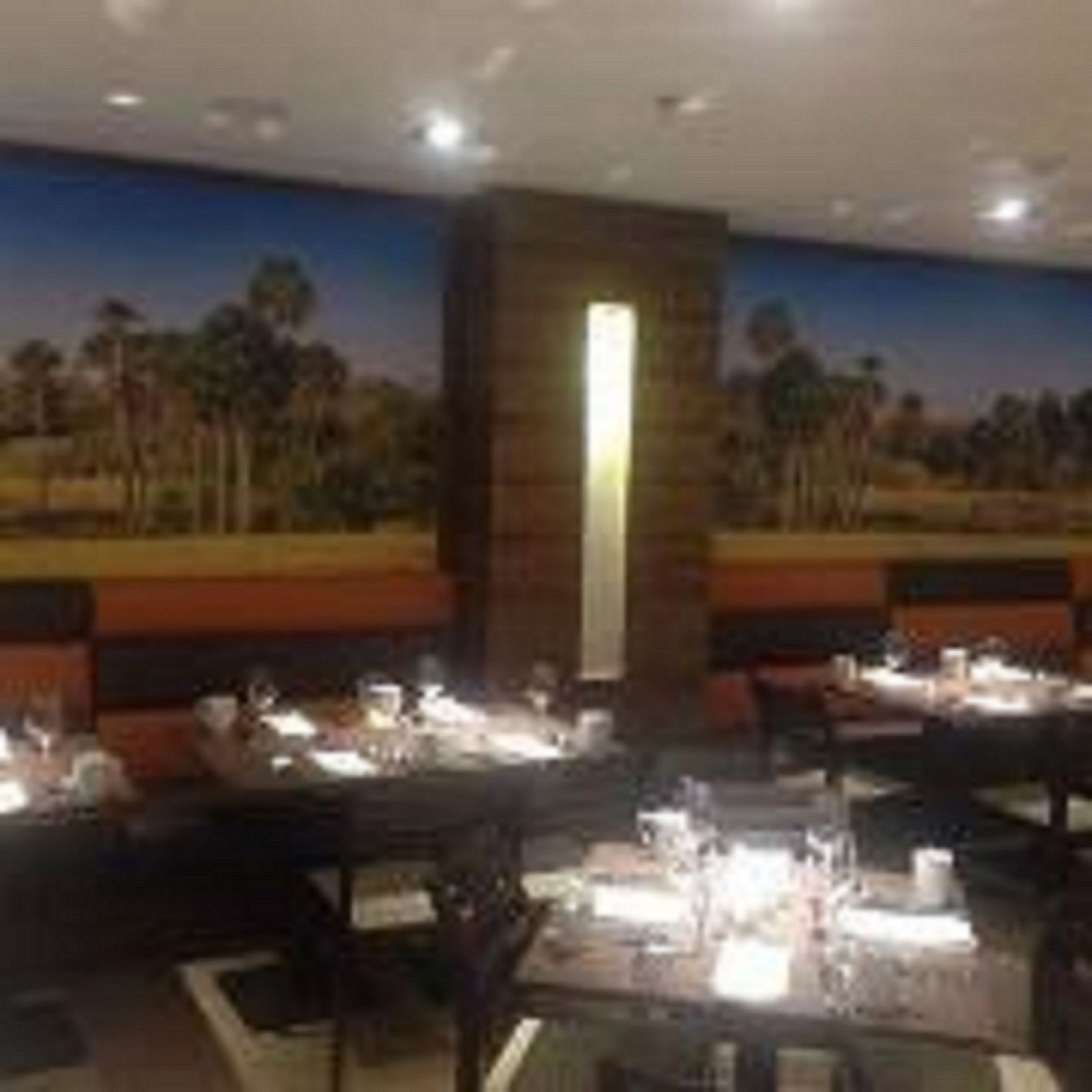 A restaurant with tables set for dining, a mural on the wall, and a pillar.