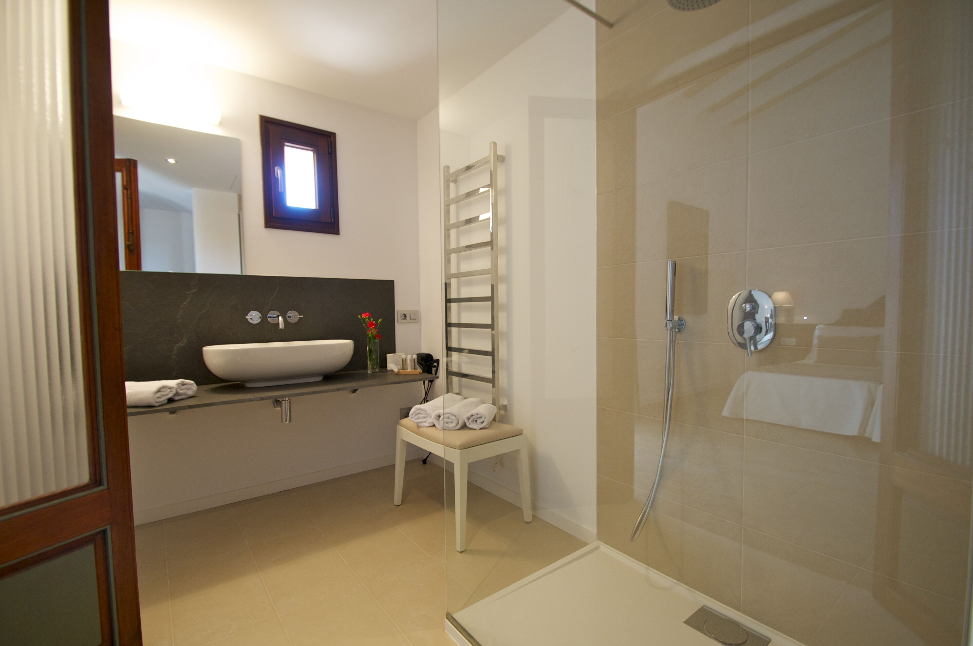 A modern bathroom with a large sink, a shower, and a chair.