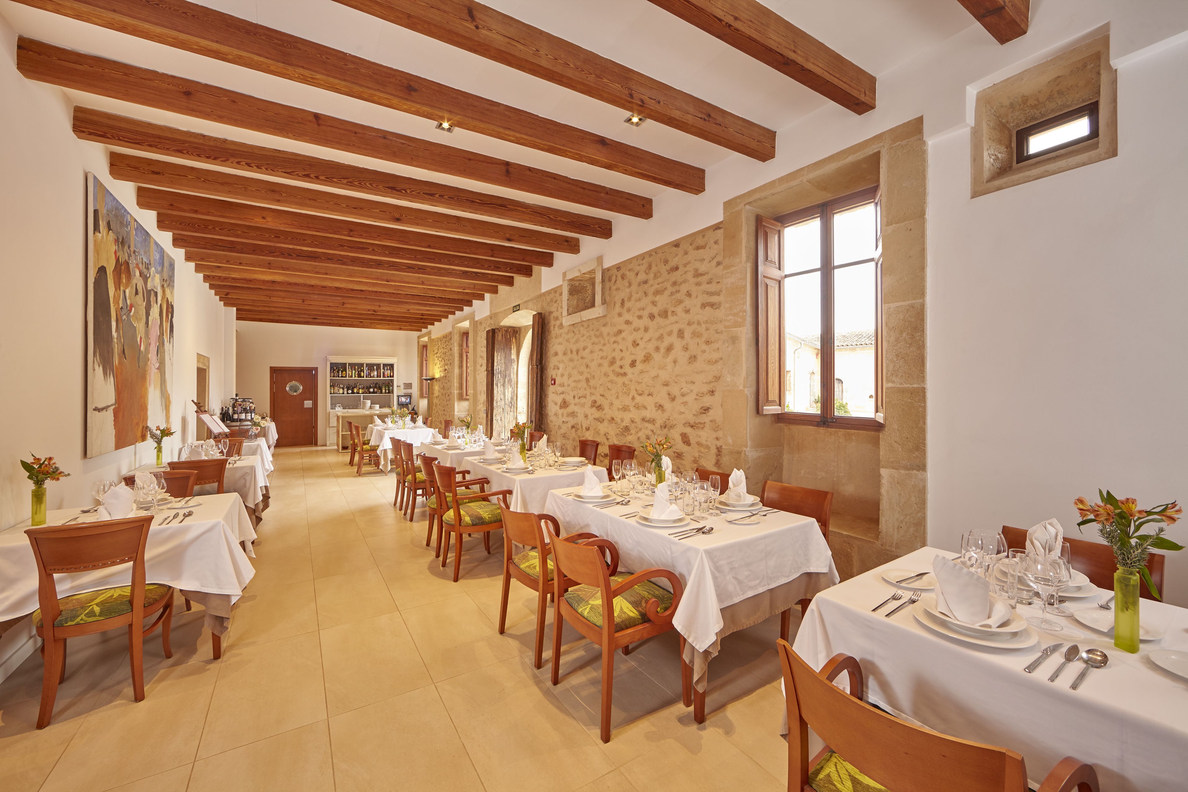 Un espace repas agrémenté de poutres en bois, de murs en pierre et de nappes blanches.