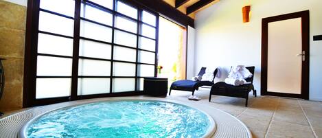Un jacuzzi en una habitación con ventanas amplias, una puerta y dos sillones de descanso.