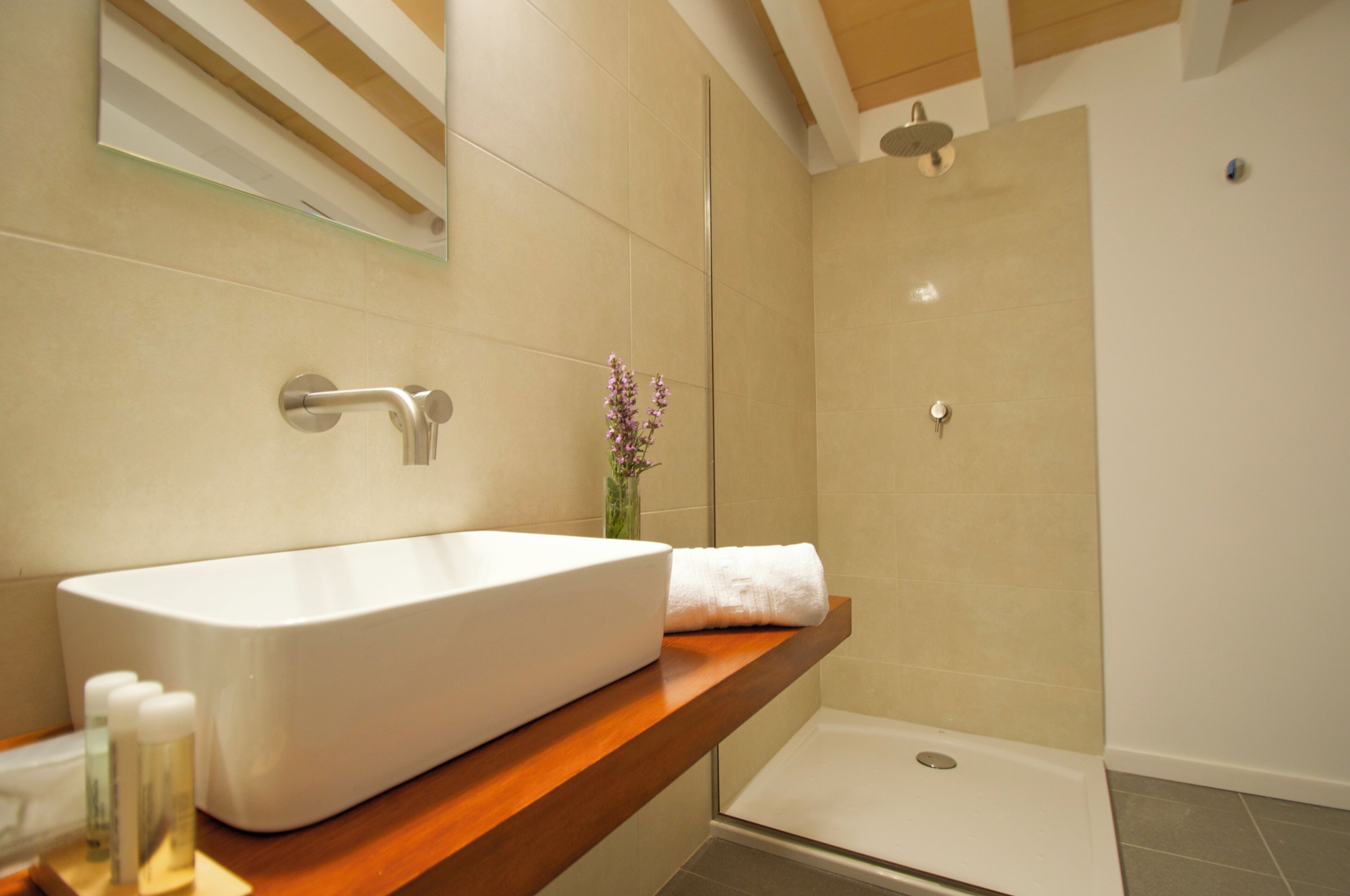 A bathroom with a large white sink, a wooden countertop, a mirror, and a shower area.