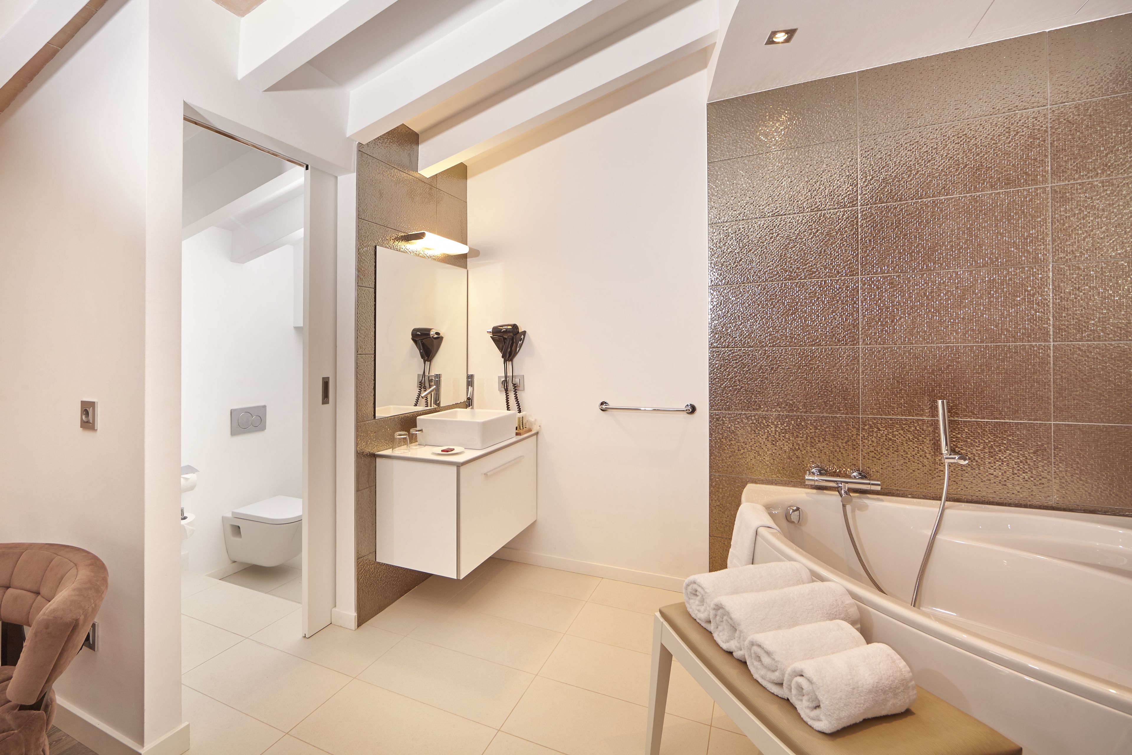 A modern bathroom with a bathtub, a sink, and a toilet. There is a bench with towels and a mirror above the sink.