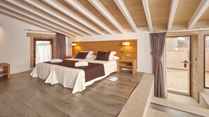 A modern hotel room with a large bed, wooden ceiling beams, a small bedside table, and a view of the outside balcony. - Bennoc Petit Hotel (Llucmajor)