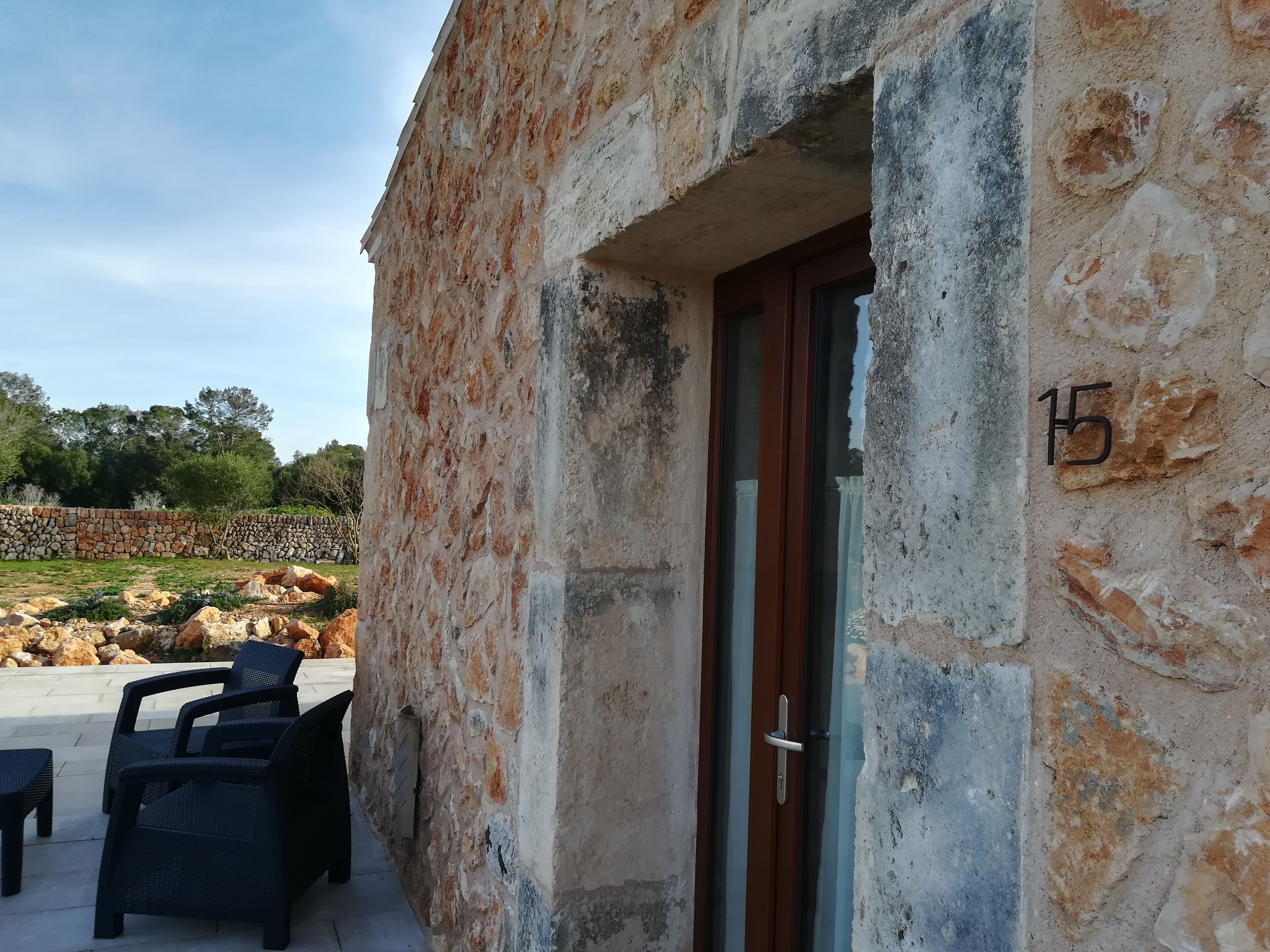 A stone building with a door marked '15', outdoor seating, and a stone wall in the background.