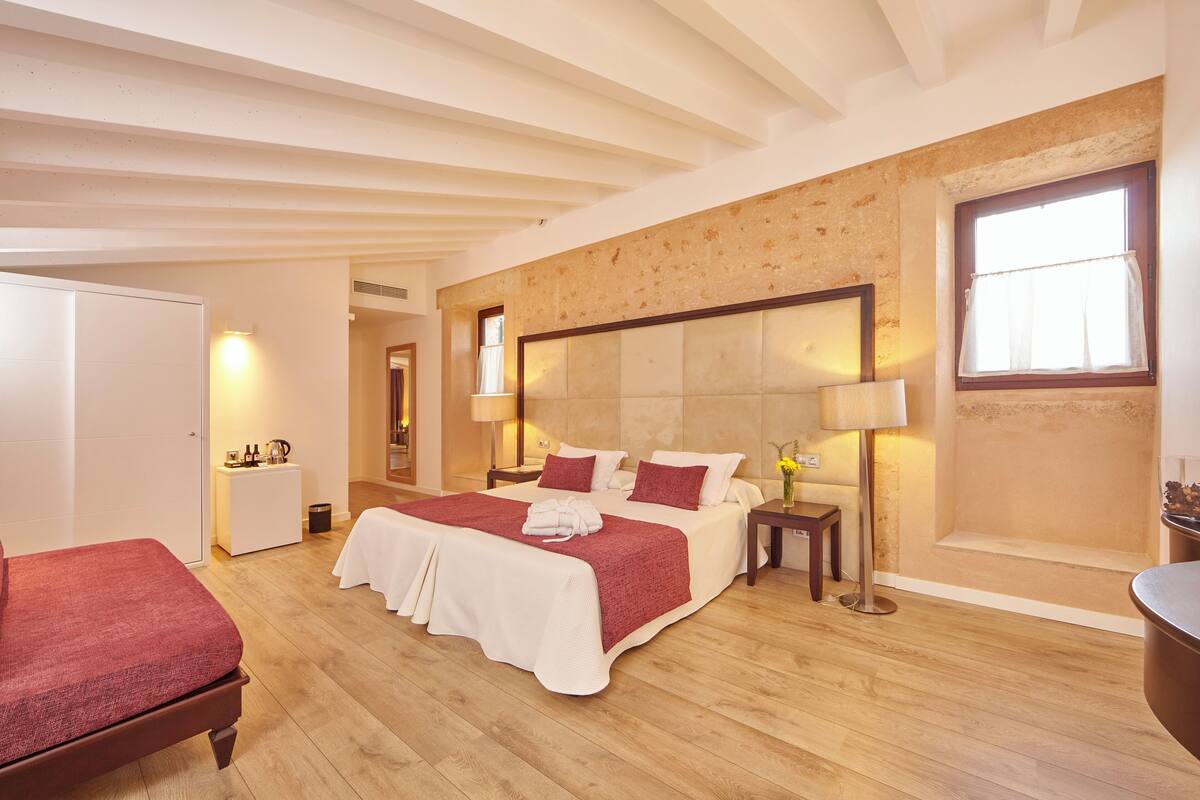 A spacious bedroom with a large bed, bedside tables, a bedside lamp, and a view of the outside through a window.