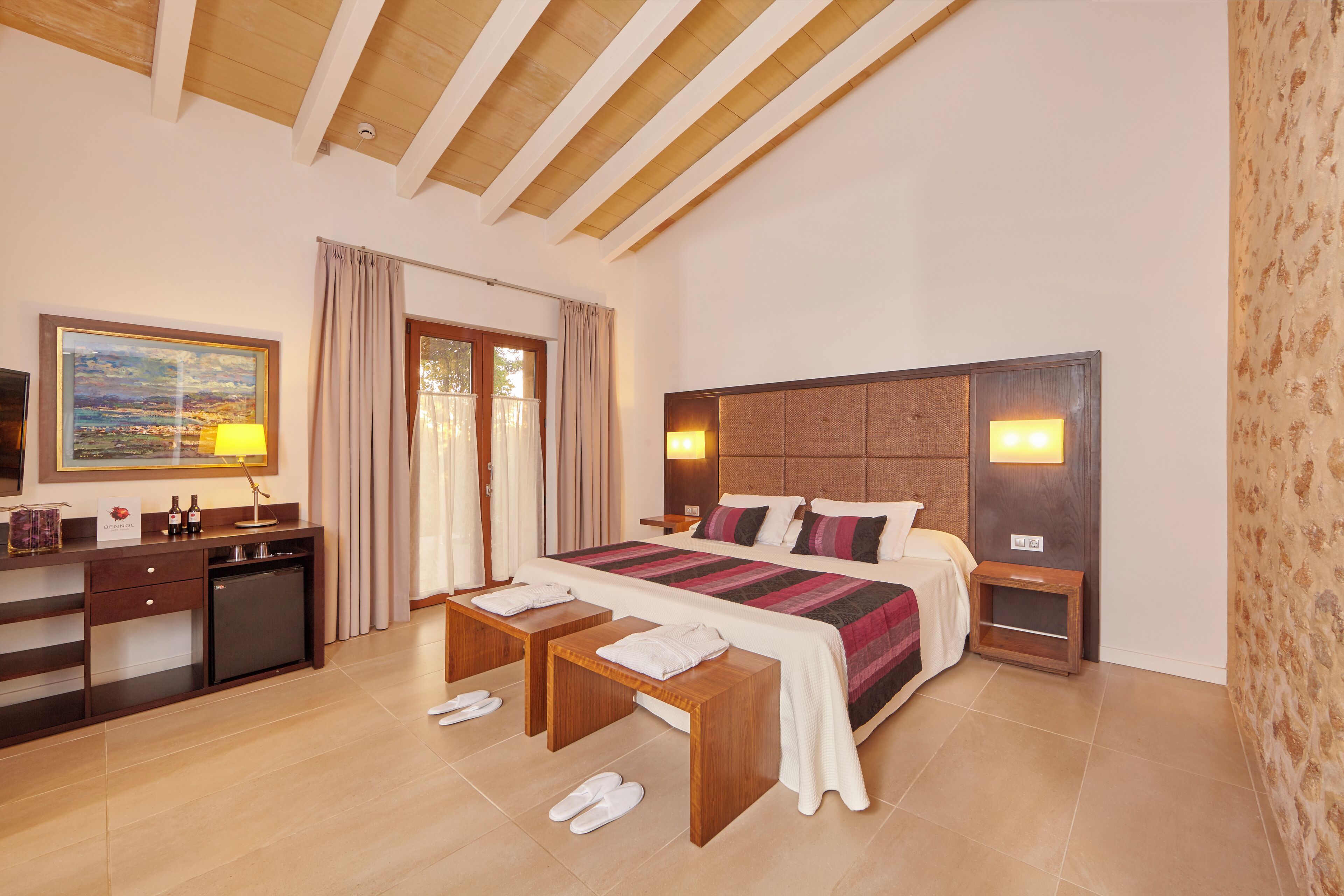A hotel room with a large bed, bedside tables, a desk with a refrigerator, and a window with curtains.