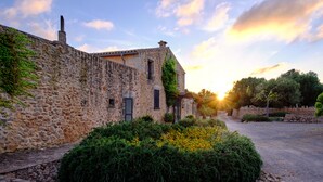 A stone building with a garden in front, a paved area, and a clear sky. - Bennoc Petit Hotel (Llucmajor)