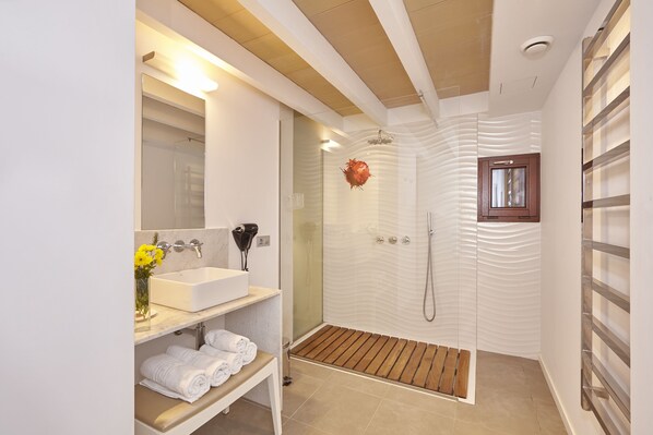 Un baño moderno con cabina de ducha de vidrio, un lavabo blanco y un mueble de tocador de madera.