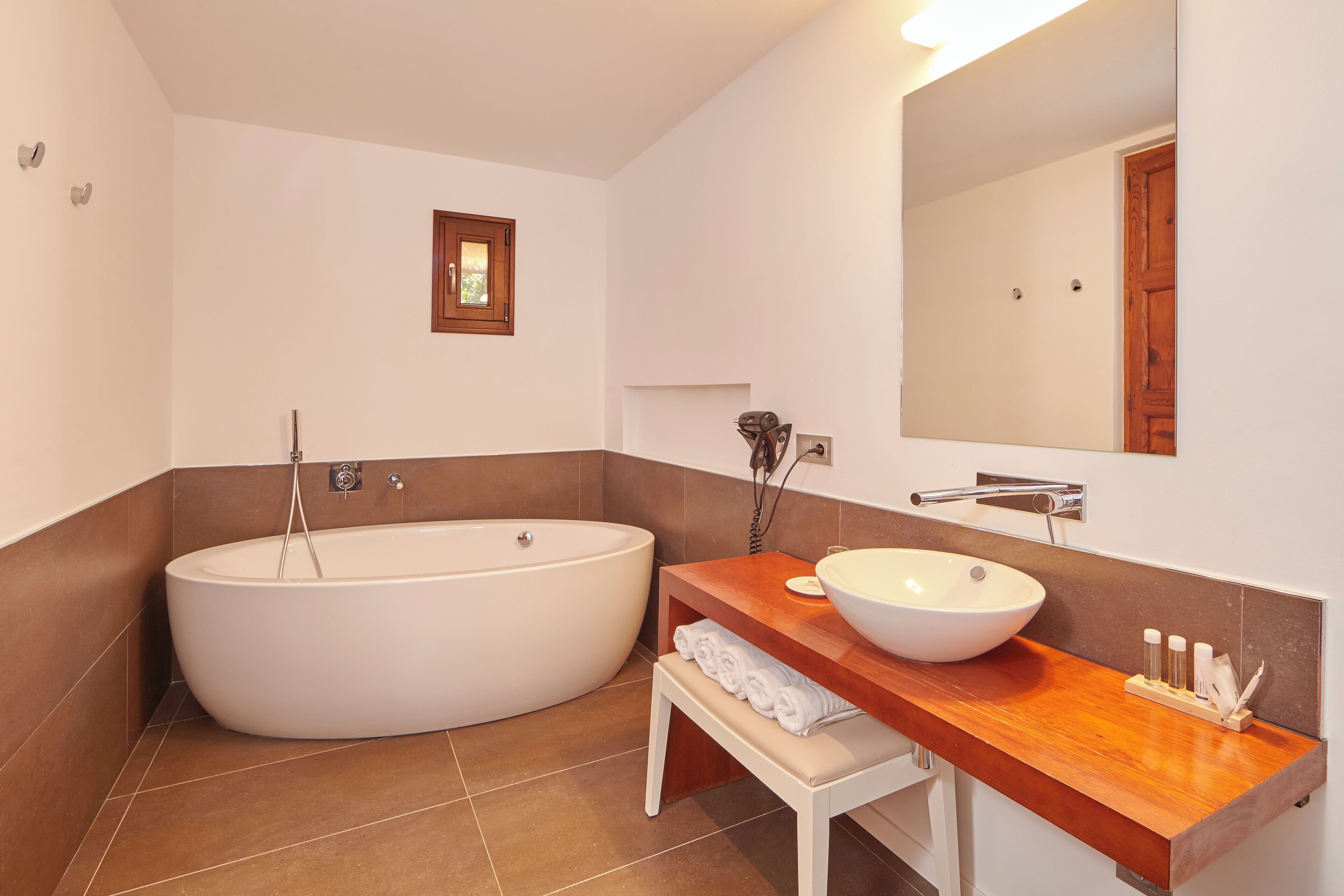 A modern bathroom with a freestanding bathtub, a wooden vanity with a large sink, and a small bench with towels.