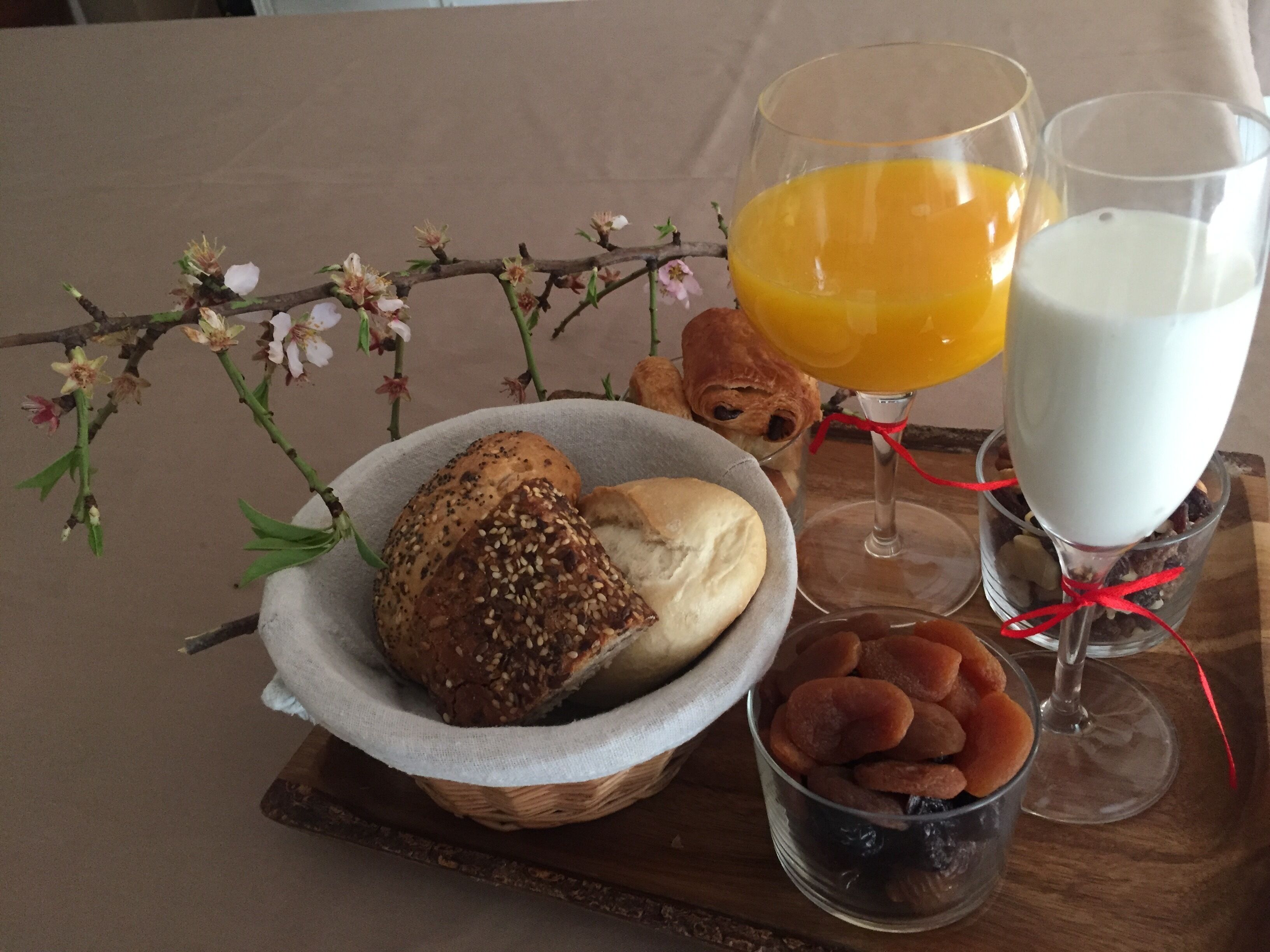 A breakfast setting with bread, a bowl of dried fruits, a glass of orange juice, and a glass of milk on a wooden table.