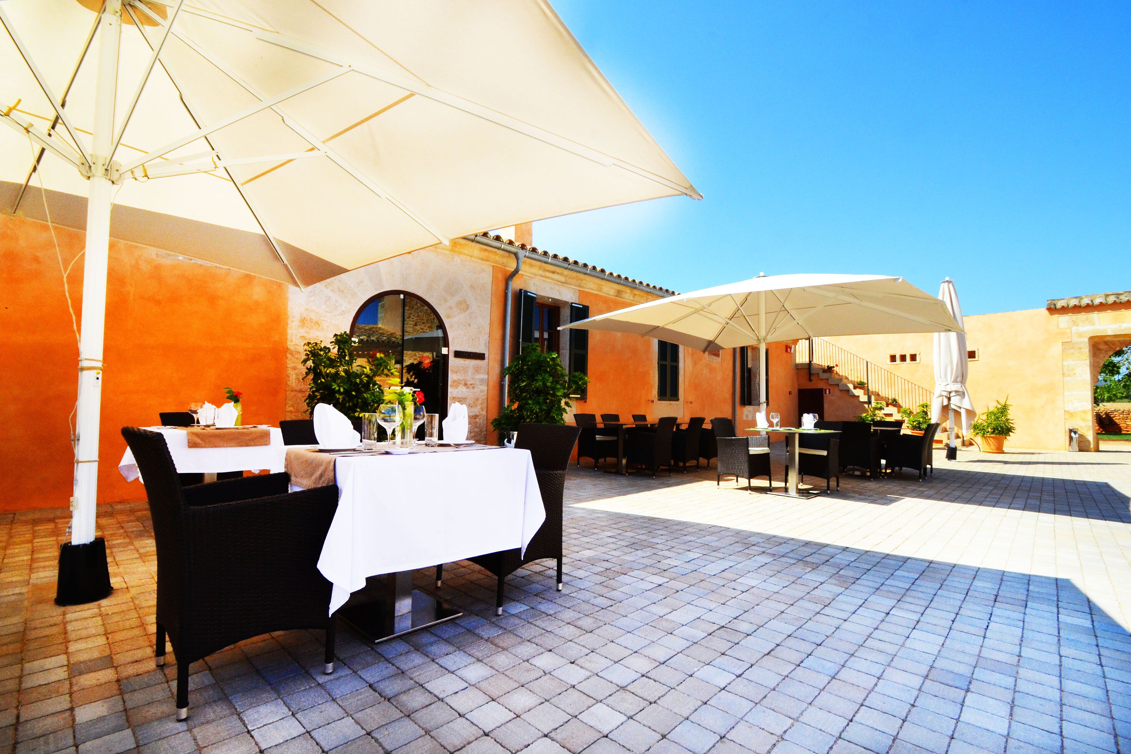Un espace de restauration en plein air, avec des tables et des chaises, protégé par de grands parasols, et un escalier menant à un niveau supérieur.
