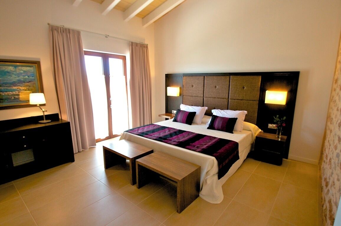 A hotel room with a large bed, bedside tables, a bench, a TV, and a painting on the wall.