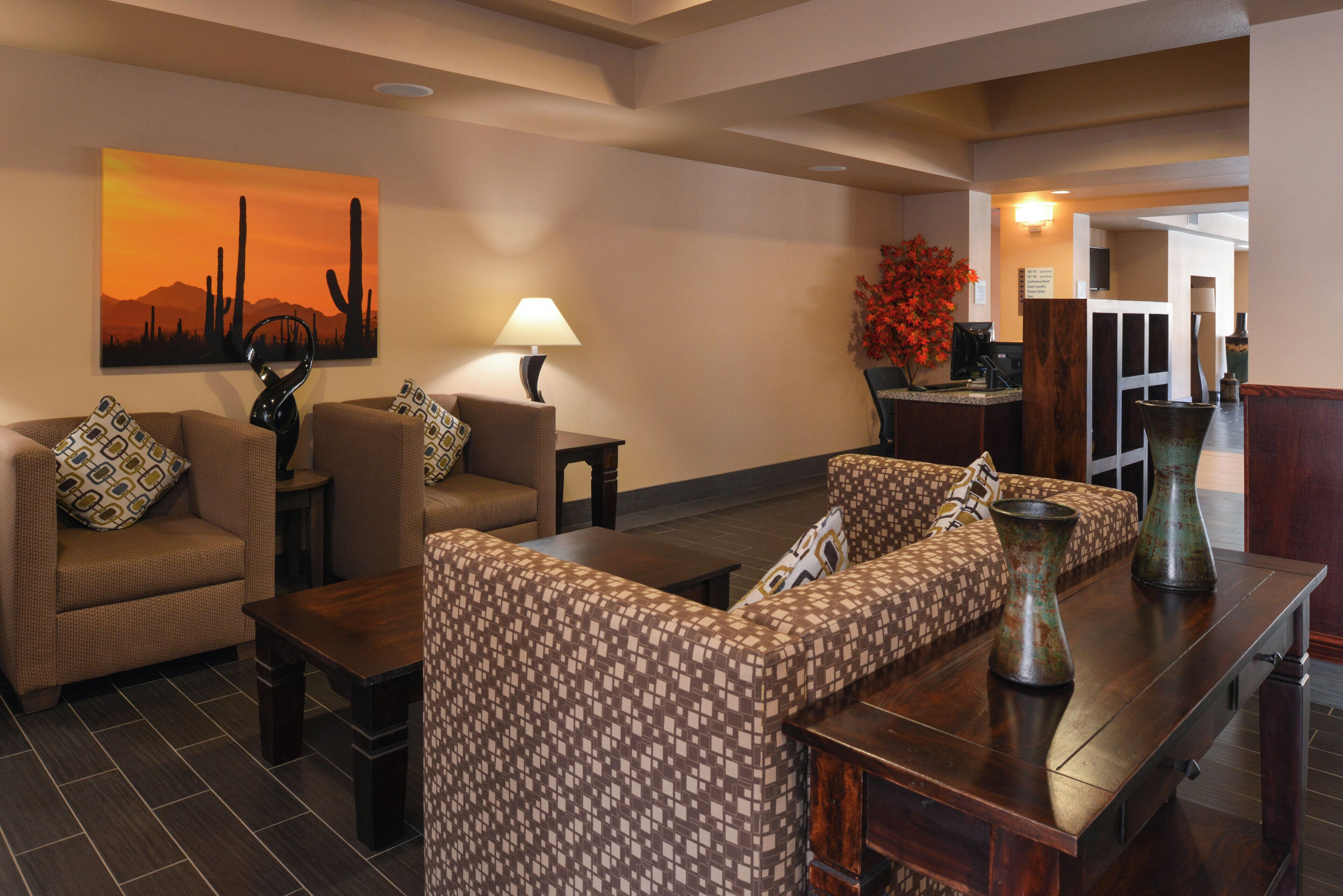 A hotel lobby with sofas, a coffee table, a lamp, a painting, and a reception desk.