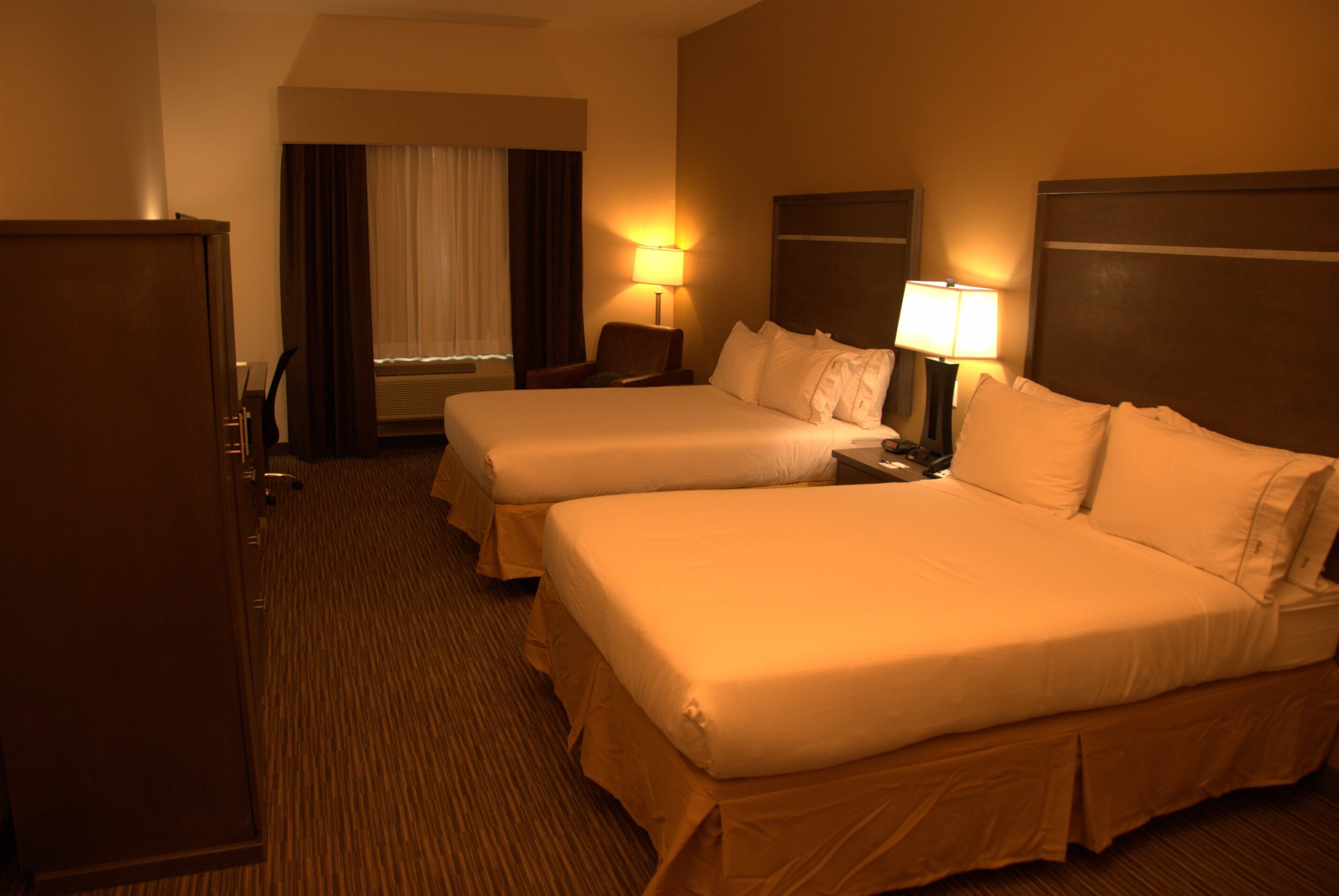 A hotel room with two beds, a desk, a chair, and a wardrobe.