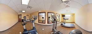 Un gimnasio con máquinas de cardio, un espejo y un reloj en la pared.