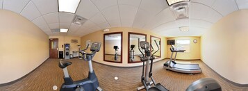 Un gimnasio con máquinas de cardio, un espejo y un reloj en la pared.