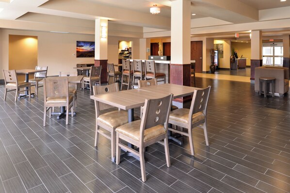 A spacious dining area with multiple tables and chairs, a modern interior design, and a view of the kitchen area in the background.
