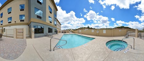 A hotel with a swimming pool, lounge chairs, and a covered patio area.
